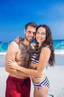 Happy couple embracing at the beach and looking at camera