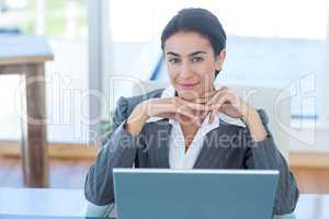 Businesswoman looking at camera and using her laptop