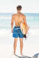 Wear view of handsome man holding surfboard