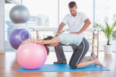 Trainer working with woman on exercise ball