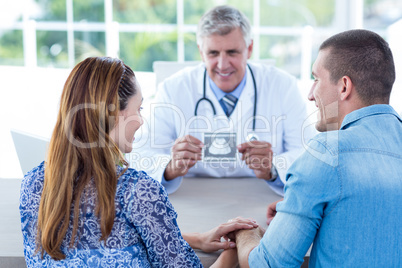 Smiling doctor showing ultrasound scan to the couple