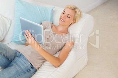 Smiling blonde woman using digital tablet on the sofa