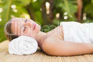 Peaceful blonde lying on bamboo mat with flowers