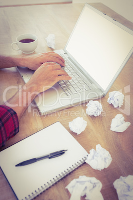 Hands typing on a laptop with paper pellets beside