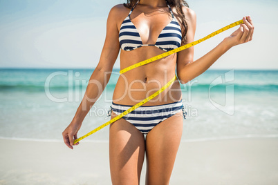 Pretty brunette measuring waist at the beach