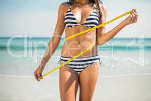 Pretty brunette measuring waist at the beach