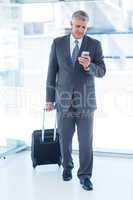 Businessman walking with luggage and using his smartphone