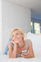 Smiling blonde woman using mobile and thinking