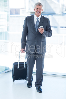 Businessman walking with luggage and using his smartphone