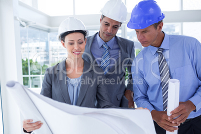 Businessmen and a woman with hard hats and holding blueprint