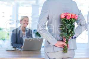 Businessman hiding flowers behind back for colleague