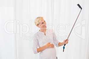 Smiling blonde pregant taking a selfie with monopod