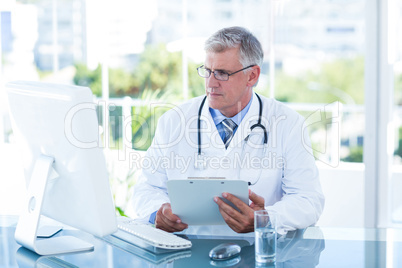 Serious doctor working on computer at his desk