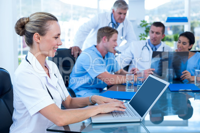 Beautiful smiling doctor typing on keyboard with her team behind