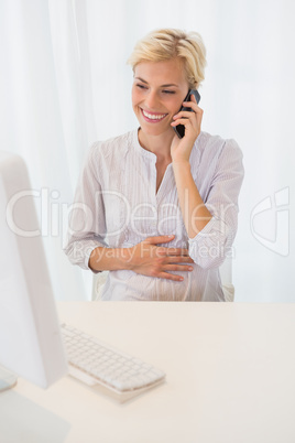 Smiling blonde woman using computer and phoning