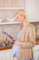 Smiling blonde pregnancy using a digital tablet