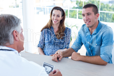 Smiling doctor showing ultrasound scan to the couple