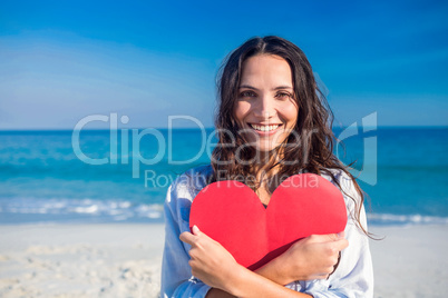 Smiling woman holding heart card at the beach