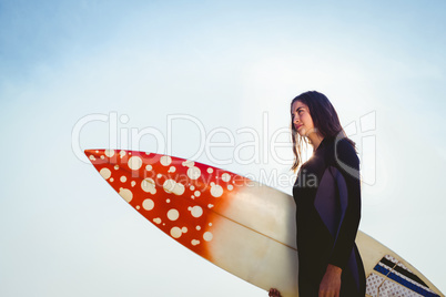 Woman in wetsuit with a surfboard on a sunny day