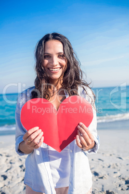 Smiling woman holding heart card at the beach