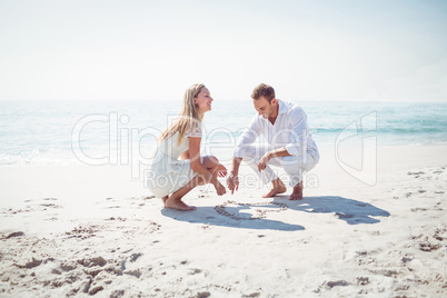 Happy couple drawing heart shape in the sand