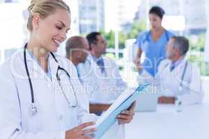 Smiling female doctor looking at clipboard while her colleagues