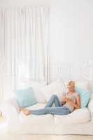Happy blonde woman using her mobile on the sofa