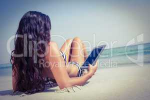 Rear view of pretty brunette using tablet pc at the beach