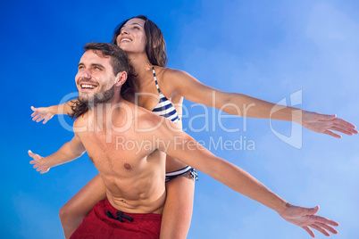 Man giving piggy back to his girlfriend at the beach