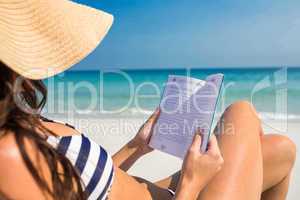 Pretty brunette reading on deck chair at the beach