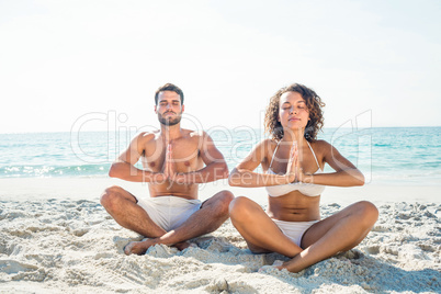 Happy couple doing yoga beside the water