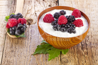 yogurt with wild berries in wooden bowl on wooden