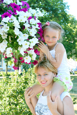 daughter sitting on her mother and many flowers in the city park
