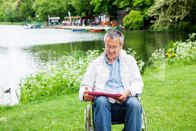 Man with wheelchair and tablet PC in the park