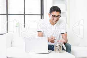 Indian guy using computer and counting money at home