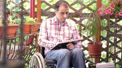 Young disabled man in wheelchair reading book