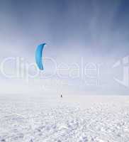 Kiteboarder with blue kite on the snow