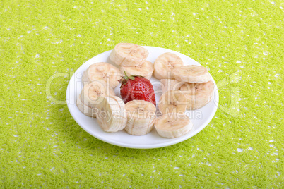 Bunch of bananas and several strawberries on white plate