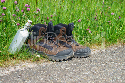 Wanderschuhe und Feldflasche am Straßenrand