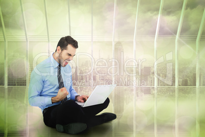 Composite image of cheering businessman sitting using his laptop