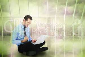 Composite image of cheering businessman sitting using his laptop