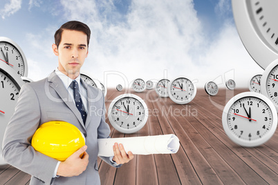 Composite image of serious architect holding plans and hard hat