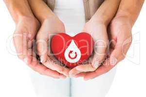 Composite image of couple holding miniature heart in hands