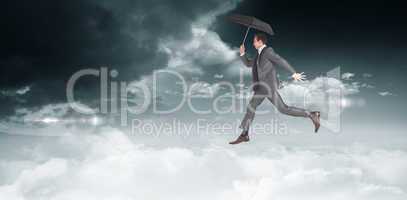 Composite image of businessman jumping holding an umbrella