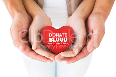 Composite image of couple holding miniature heart in hands