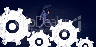 Composite image of businessman walking and holding umbrella