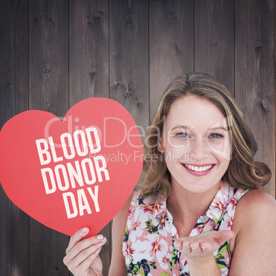 Composite image of woman holding heart card and blowing kiss