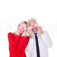 Composite image of silly couple holding hearts over their eyes