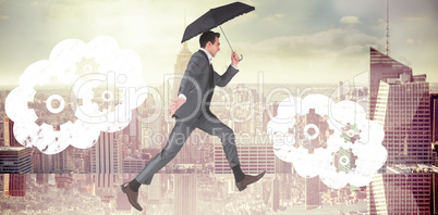 Composite image of businessman jumping holding an umbrella