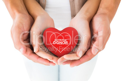 Composite image of couple holding miniature heart in hands